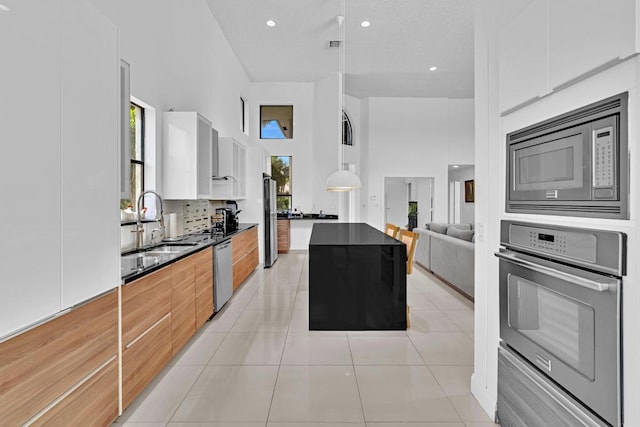 kitchen featuring sink, white cabinets, appliances with stainless steel finishes, light tile patterned floors, and a high ceiling