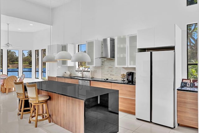 kitchen with a kitchen breakfast bar, white fridge, a center island, ceiling fan, and wall chimney range hood