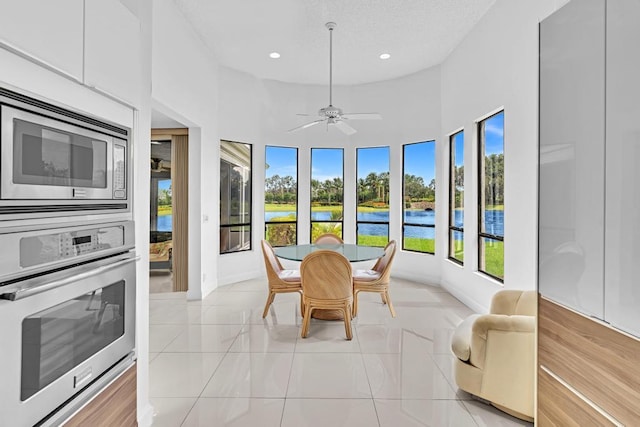 tiled dining space with ceiling fan, a towering ceiling, a water view, and a healthy amount of sunlight