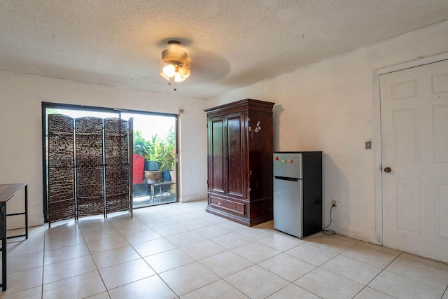 unfurnished bedroom featuring a textured ceiling, ceiling fan, light tile patterned floors, and stainless steel fridge