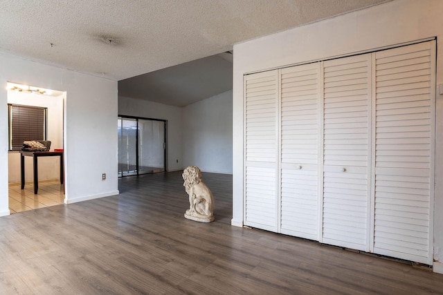 unfurnished bedroom featuring a closet, vaulted ceiling, a textured ceiling, and hardwood / wood-style floors