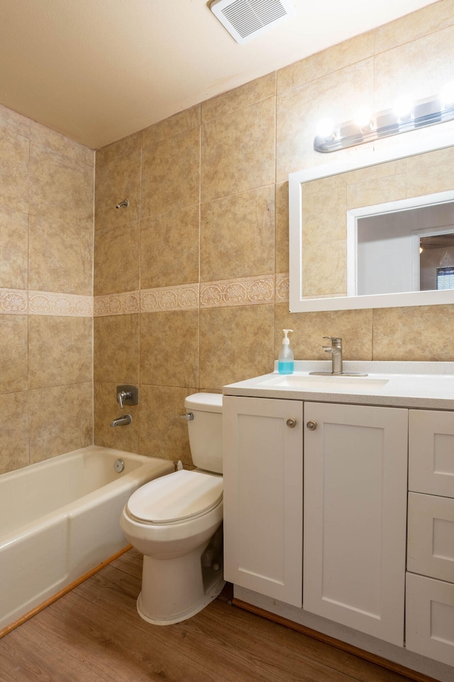 full bathroom with tile walls, vanity, hardwood / wood-style floors, shower / bathing tub combination, and toilet