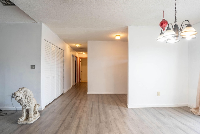 unfurnished room with an inviting chandelier, light hardwood / wood-style floors, and a textured ceiling