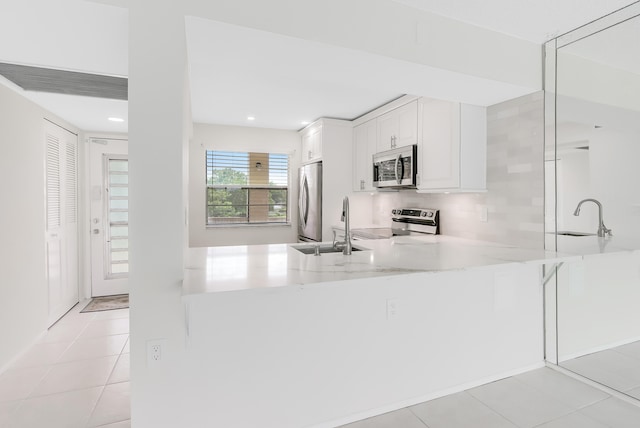 kitchen featuring appliances with stainless steel finishes, kitchen peninsula, sink, white cabinets, and light tile patterned flooring