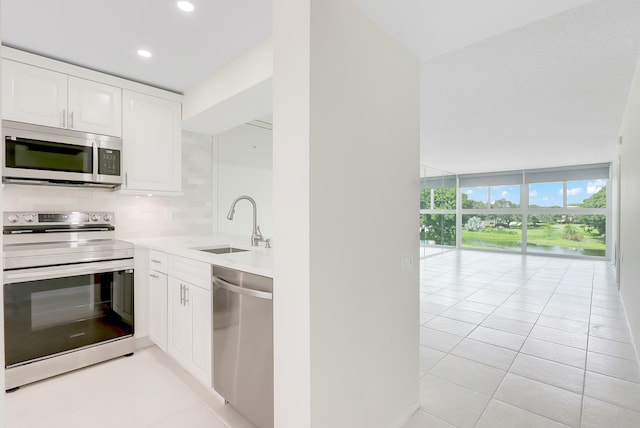 kitchen featuring a wall of windows, backsplash, appliances with stainless steel finishes, and white cabinetry