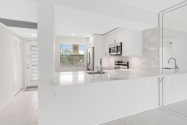 kitchen with appliances with stainless steel finishes, white cabinets, a sink, and a peninsula