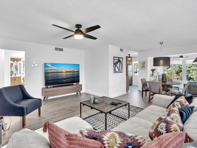 living room with a textured ceiling, light hardwood / wood-style flooring, and ceiling fan