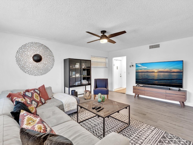 living room featuring wood-type flooring, a textured ceiling, and ceiling fan