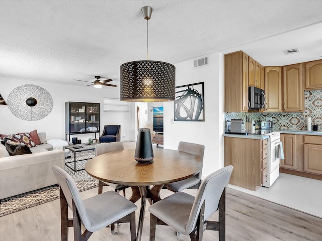 dining room with ceiling fan, light wood-type flooring, and a textured ceiling