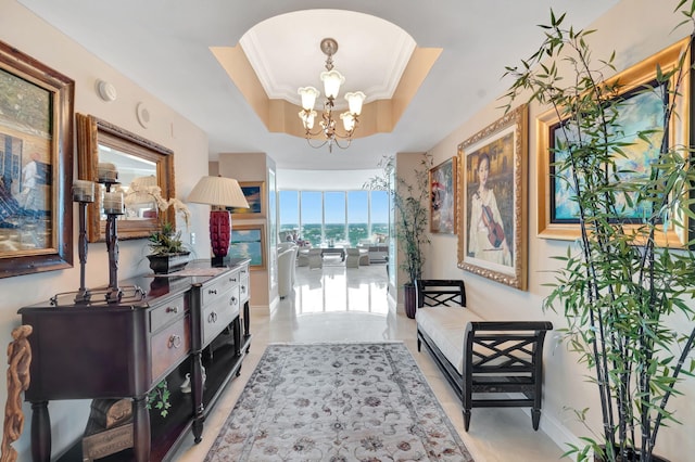 corridor with a tray ceiling, crown molding, and a chandelier