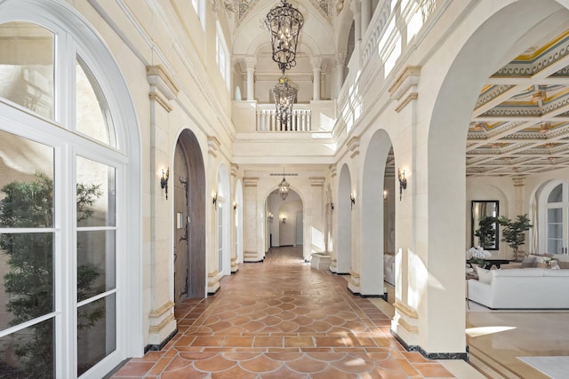 hallway featuring beamed ceiling, a notable chandelier, a high ceiling, and coffered ceiling