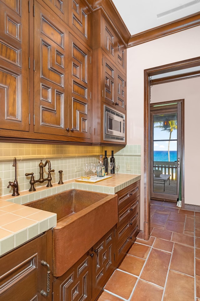 kitchen featuring stainless steel microwave, decorative backsplash, tile counters, and crown molding