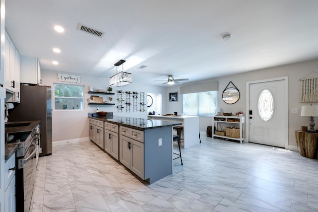 kitchen featuring a breakfast bar, gray cabinets, dark stone counters, hanging light fixtures, and ceiling fan