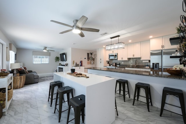 kitchen with ceiling fan, white cabinets, hanging light fixtures, stainless steel appliances, and a kitchen breakfast bar