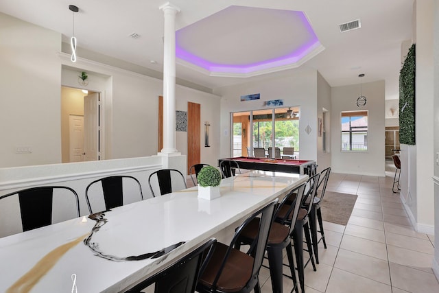 dining area with light tile patterned flooring, a tray ceiling, and ornate columns