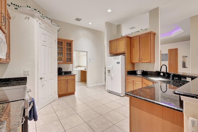 kitchen featuring stove, sink, kitchen peninsula, white fridge with ice dispenser, and dark stone counters