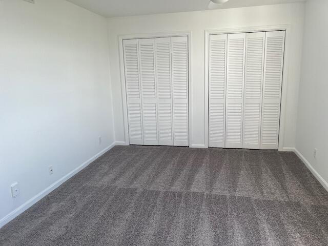 unfurnished bedroom with multiple closets and dark colored carpet