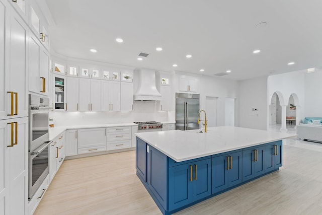 kitchen featuring custom exhaust hood, white cabinets, a spacious island, blue cabinetry, and stainless steel appliances