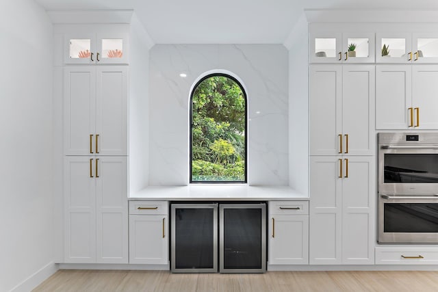 kitchen featuring backsplash, wine cooler, white cabinetry, and stainless steel double oven