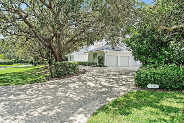 view of front of house featuring a garage, a tiled roof, decorative driveway, stucco siding, and a front yard