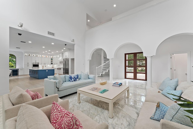 living room with a towering ceiling, decorative columns, a healthy amount of sunlight, and sink