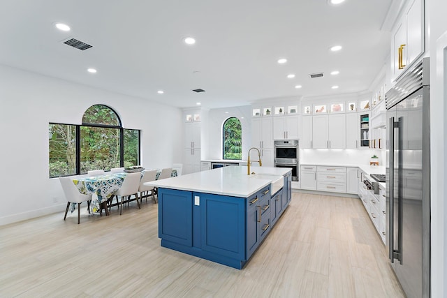 kitchen featuring blue cabinets, white cabinets, light countertops, and glass insert cabinets