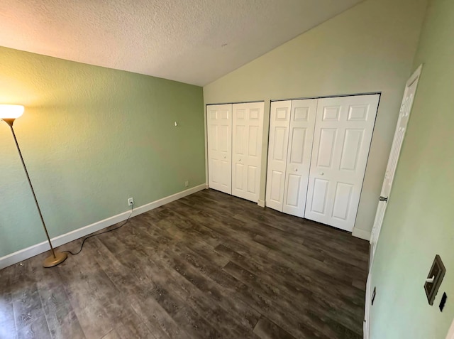 unfurnished bedroom with multiple closets, a textured ceiling, lofted ceiling, and dark wood-type flooring