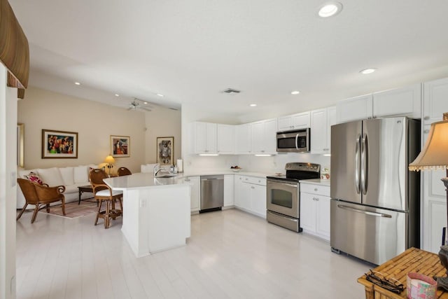 kitchen with white cabinetry, kitchen peninsula, sink, appliances with stainless steel finishes, and light hardwood / wood-style floors