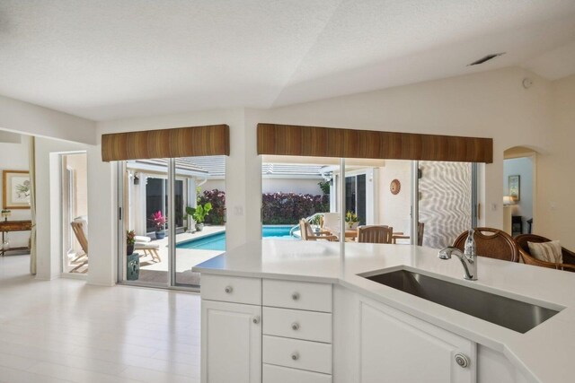 kitchen featuring a textured ceiling, vaulted ceiling, light hardwood / wood-style floors, sink, and white cabinets