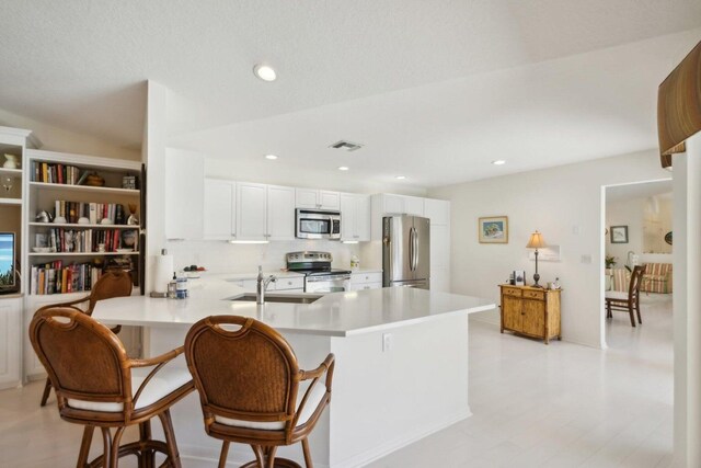 kitchen featuring a breakfast bar area, kitchen peninsula, sink, stainless steel appliances, and white cabinets