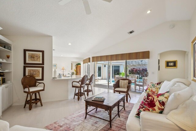 living room featuring lofted ceiling, ceiling fan, light wood-type flooring, and a textured ceiling