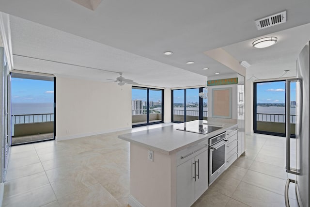 kitchen featuring ceiling fan, a wall of windows, white cabinets, a water view, and appliances with stainless steel finishes