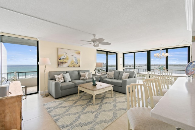 tiled living room with ceiling fan with notable chandelier, a water view, a wall of windows, and a textured ceiling