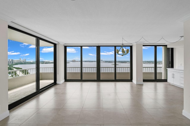 tiled spare room with a water view, a wall of windows, and a textured ceiling