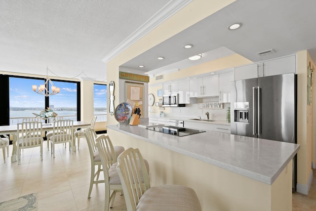 kitchen featuring visible vents, crown molding, appliances with stainless steel finishes, a kitchen breakfast bar, and a sink