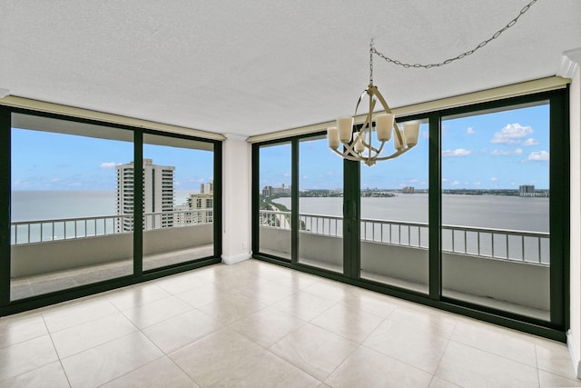 unfurnished room featuring a wall of windows, a water view, a textured ceiling, and an inviting chandelier