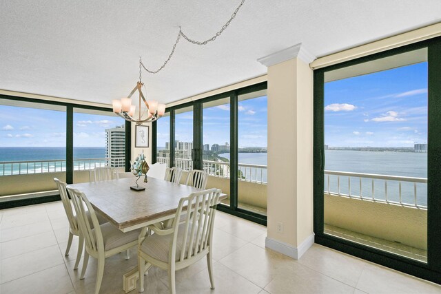 tiled dining space with a textured ceiling, a water view, an inviting chandelier, and a wall of windows