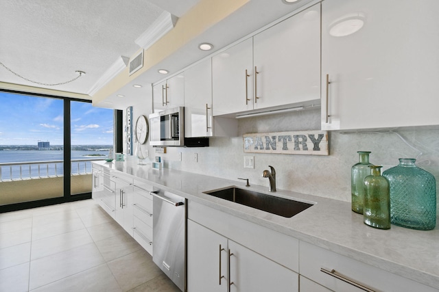 kitchen featuring backsplash, a water view, white cabinetry, and sink