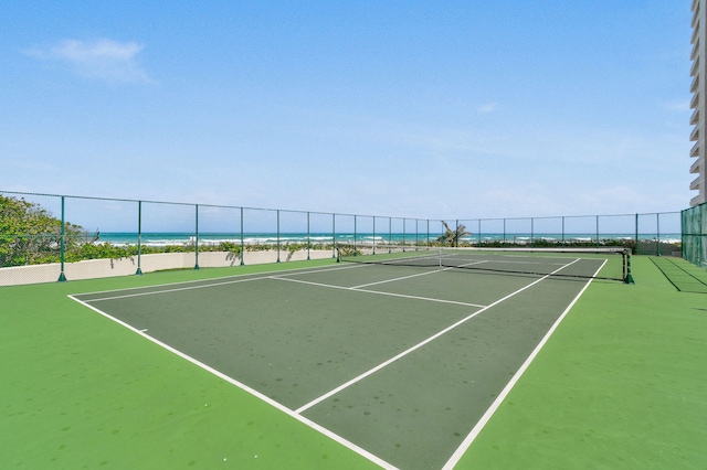 view of sport court featuring a water view, a view of the beach, and fence