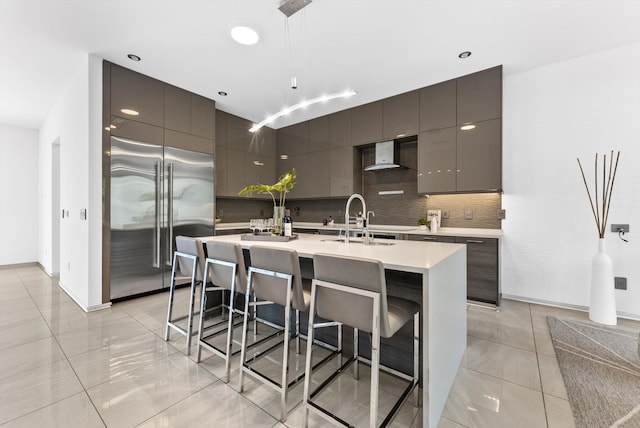 kitchen featuring sink, backsplash, built in fridge, a kitchen breakfast bar, and wall chimney exhaust hood