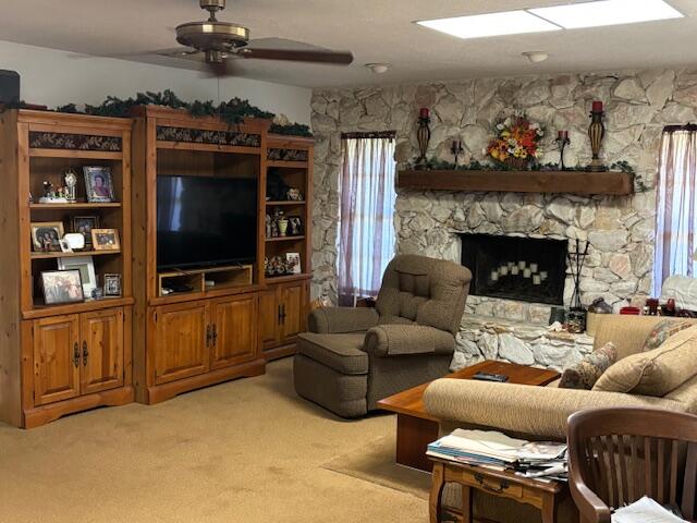 carpeted living room with ceiling fan, a stone fireplace, and plenty of natural light