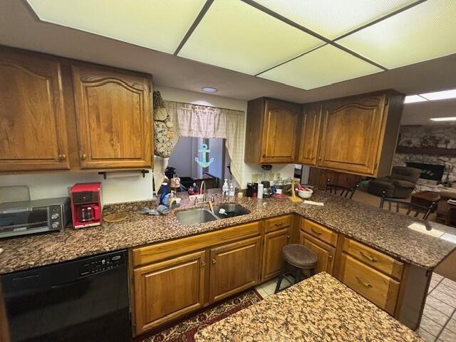 kitchen with a stone fireplace, dishwasher, sink, and stone countertops