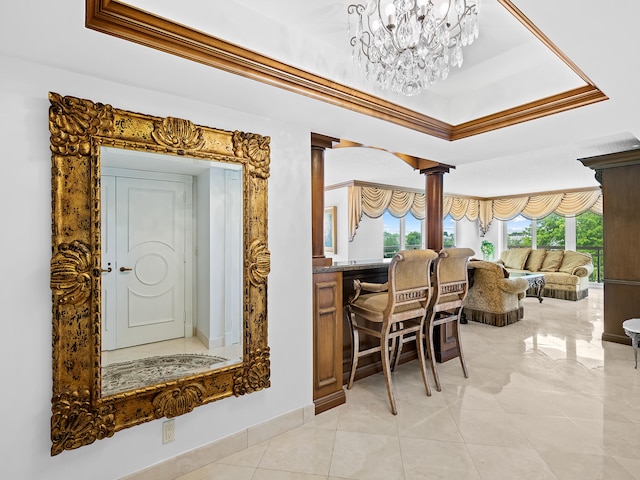 dining area with decorative columns, an inviting chandelier, and a raised ceiling