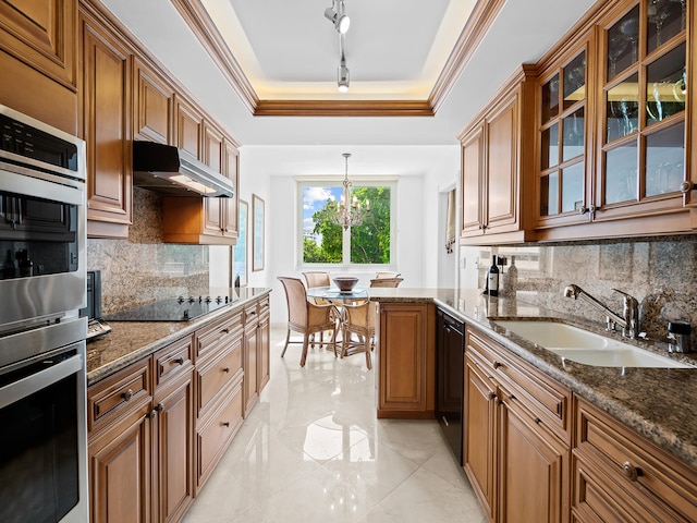 kitchen featuring a raised ceiling, hanging light fixtures, sink, black appliances, and dark stone countertops