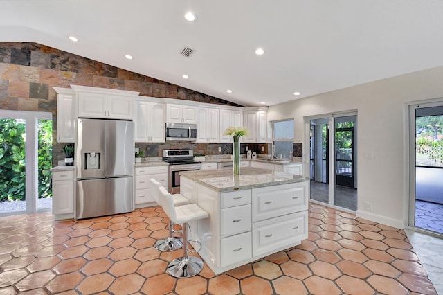 kitchen with light stone counters, stainless steel appliances, white cabinets, a kitchen island, and lofted ceiling