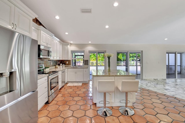 kitchen with stainless steel appliances, tasteful backsplash, white cabinets, a kitchen breakfast bar, and a kitchen island