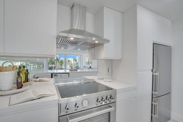 kitchen with wall chimney range hood, white cabinetry, and stainless steel appliances