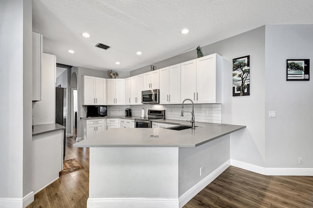 kitchen featuring kitchen peninsula, appliances with stainless steel finishes, sink, white cabinets, and dark hardwood / wood-style floors