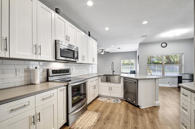 kitchen with white cabinetry, sink, light hardwood / wood-style flooring, kitchen peninsula, and appliances with stainless steel finishes