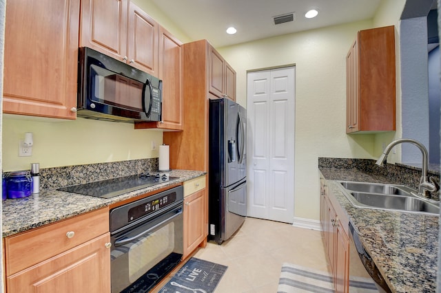 kitchen with sink, light tile patterned floors, black appliances, and dark stone counters